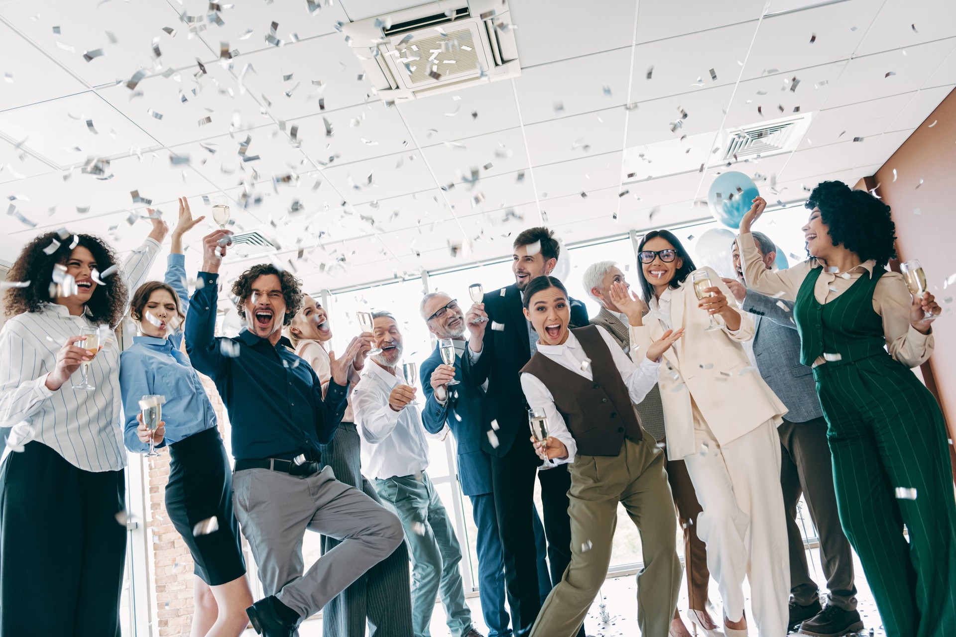 Diverse group of professionals celebrating in an office environment with confetti and champagne, showcasing teamwork